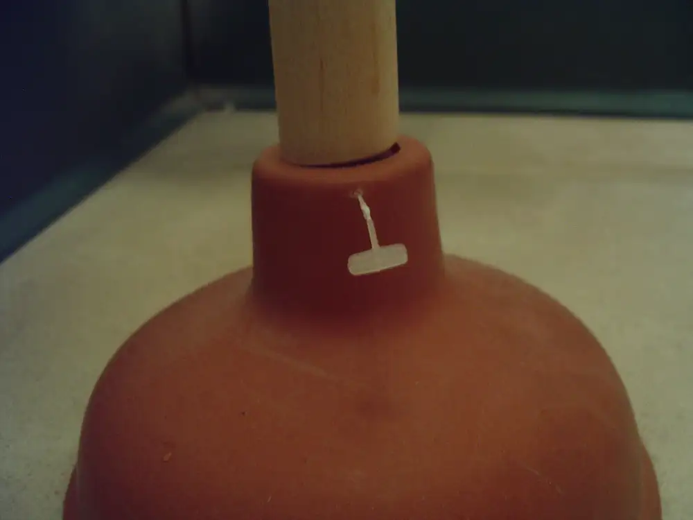 Desatascador de ventosa de goma con mango de madera apoyado en el suelo
