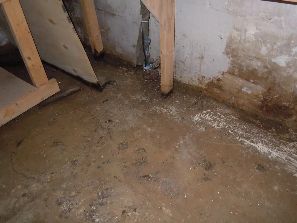 Suelo de un sótano encharcado y manchado por una fuga de agua, con montantes de madera junto a la pared