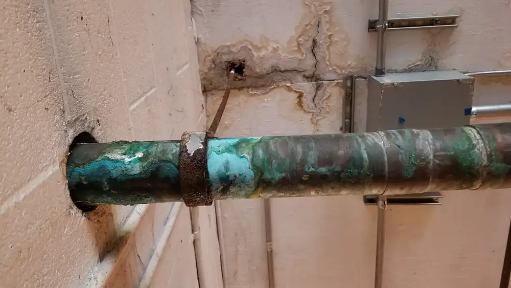 Tubería de cobre corroída y con manchas verdes que sale de una pared con marcas de humedad
