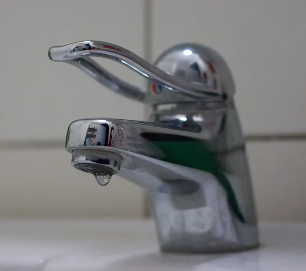 Grifo monomando cromado de lavabo con una gota de agua cayendo del caño