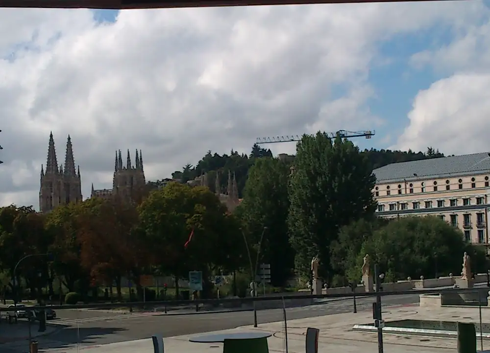 Vista de Burgos con las agujas de la catedral al fondo, arboleda y edificios junto a una avenida
