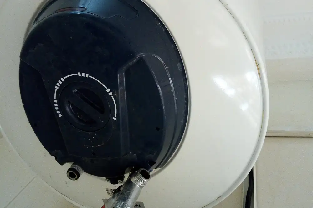 Parte inferior de un termo eléctrico blanco colgado en la pared, con la tapa del termostato y la toma de agua